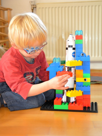 Child with model rocket built from empty toilet tissue rolls and a service structure built out of plastic building blocks.